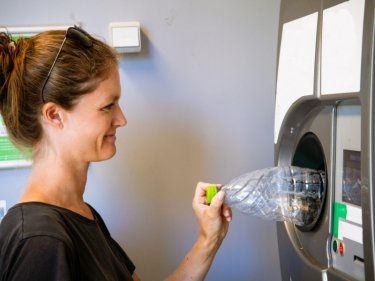 Frau gibt Plastik-Pfandflasche an Automat zurück